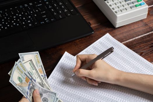 Obligation to pay wages and debts in the company.A cashier holds money dollars over an office work space with documents, a cash register, a phone, and a computer.Work in the office with finances