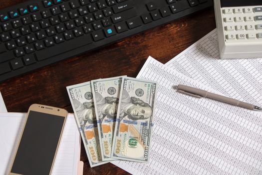 Money dollars are on the desktop in the office next to the computer, phone, documents and cash register.Obligation to pay wages and debts in the company.Work in the office with finances and documents