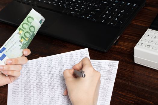 Work in the office with finance. A cashier holds money Euro over an office workspace with documents,a cash register, a phone, and a computer.Obligation to pay wages and debts in the company in Europe