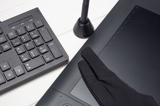 Graphic tablet, digital tablet and special pen, glove and keyboard on a white wooden table. Close-up, top view, flat lay. Freelance, designer, Illustrator. Technology, remote work, outsourcing. 