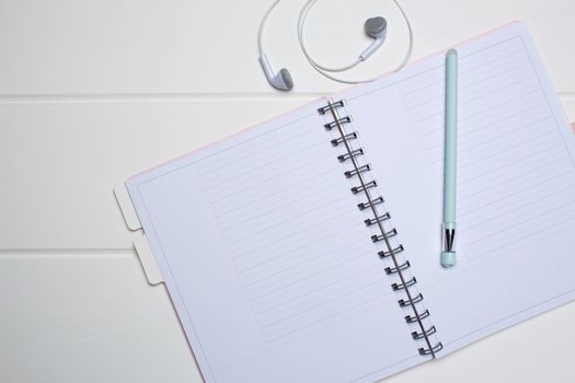 Daily planner on a white wooden background. Close-up, copy space, clear space, mockup. Clean sheet, flat lay, top view. Notepad, pen, headphones