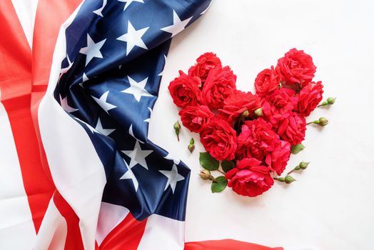 Independence Day USA concept. Memorial Day. Heart shape of red roses with the US flag flat lay top view