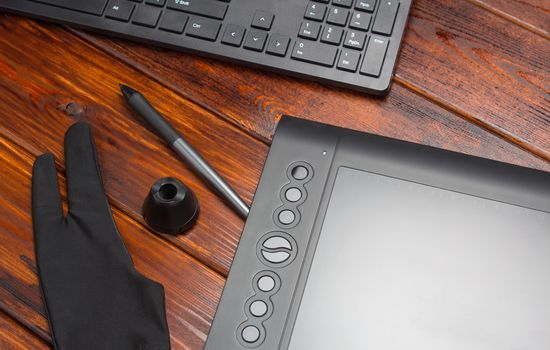Graphic tablet, digital tablet and special pen, glove and keyboard on a wooden table. Close-up, top view, flat lay. Freelance, designer, Illustrator. Technology, remote work, outsourcing. concept