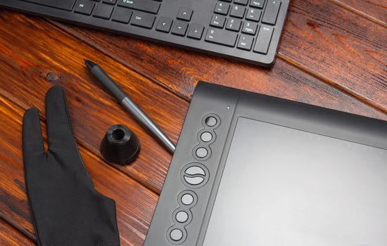 Graphic tablet, digital tablet and special pen, glove and keyboard on a wooden table. Close-up, top view, flat lay. Freelance, designer, Illustrator. Technology, remote work, outsourcing. concept