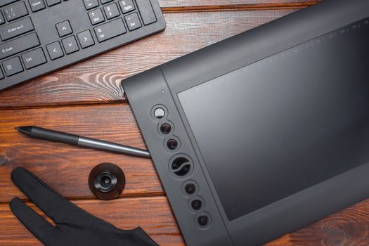 Graphic tablet, digital tablet and special pen, glove and keyboard on a wooden table. Close-up, top view, flat lay. Freelance, designer, Illustrator. Technology, remote work, outsourcing. Project,