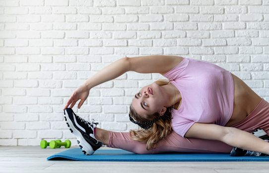 Fitness, sport, training and lifestyle concept. Sportive caucasian woman stretching at the training mat at home. Front view