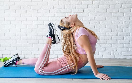 Fitness, sport, training and lifestyle concept. Sportive caucasian woman stretching at the training mat at home. Front view with copy space