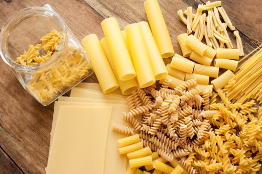 Selection of assorted dried Italian pasta in different shapes arranged in a layer on a wooden table viewed from above