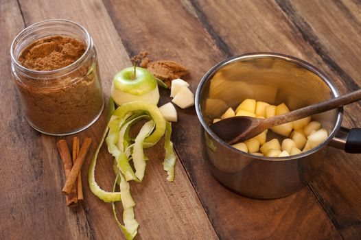 Preparing an apple sauce for christmas with diced fresh green fruit in a metal saucepan and a jar of spicy cinnamon on a wooden table