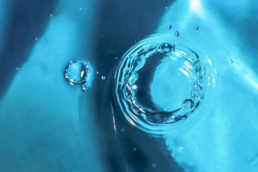 Water splash close-up. Drop of water. Blue water drop. Falling blue water surface with splash and air bubbles