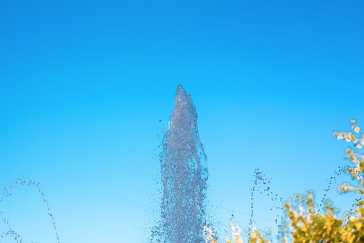 A jet of water against the blue sky. Splashes and drops of water on the fountain in the Park.