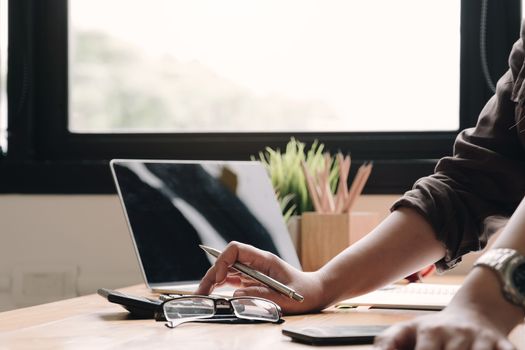 Close up Business woman using calculator and laptop for do math finance on wooden desk in office and business working background, tax, accounting, statistics and analytic research concept
