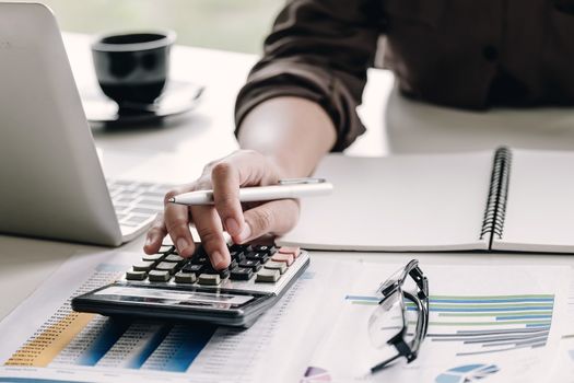 Close up Business woman using calculator and laptop for do math finance on wooden desk in office and business working background, tax, accounting, statistics and analytic research concept
