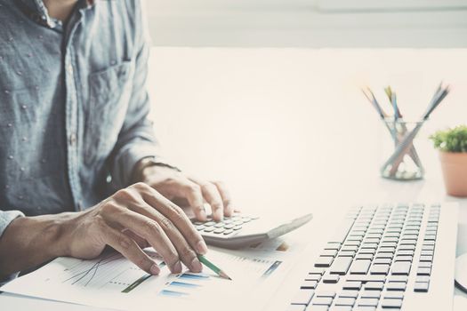 Close up of businessman or accountant hand holding pen working on calculator to calculate business data, accountancy document and laptop computer at office, business concept
