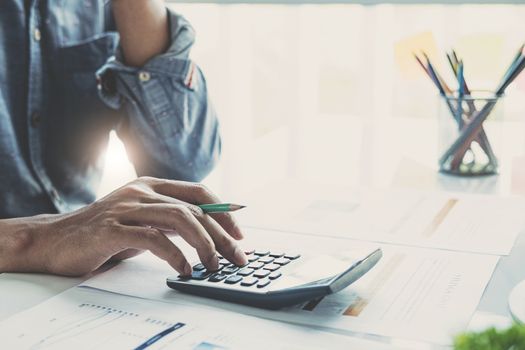 Close up of businessman or accountant hand holding pen working on calculator to calculate business data, accountancy document and laptop computer at office, business concept
