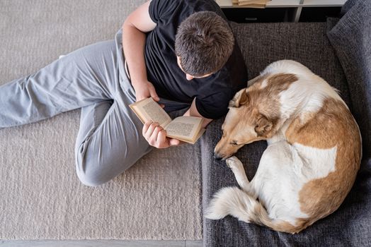 Stay home. Pet care. Young man reading sitting on the floor at home with his dog