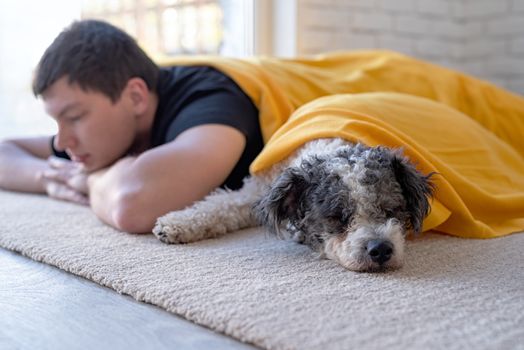 Stay home. Pet care. Young man sleeping with his bichon frise dog on the floor