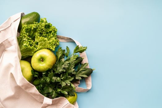 Coronavirus food supplies concept. Food layout with apples, lettuce, cucumbers, limes, parsley in eco friendly bag on blue background. Flat lay. Copy space.