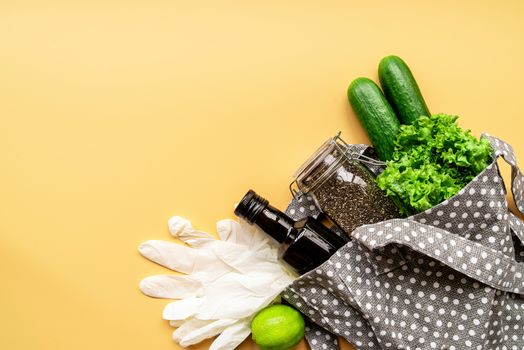 Coronavirus food supplies concept. Food layout with green vegetables, lettuce, olive oil, chia seeds, gloves in eco friendly bag on orange background. Flat lay. Copy space.