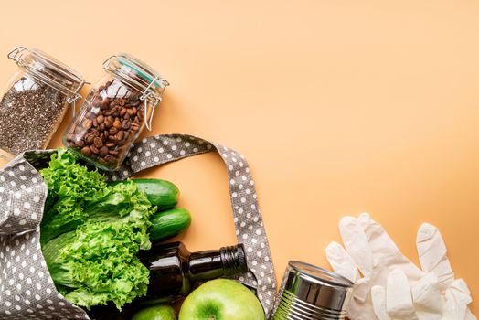 Coronavirus food supplies concept. Food layout with green vegetables, lettuce, olive oil, chia seeds, gloves in eco friendly bag on orange background. Flat lay. Copy space.