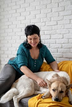 Stay home. Pet care. Middle aged woman patting her shepherd dog on the sofa at home