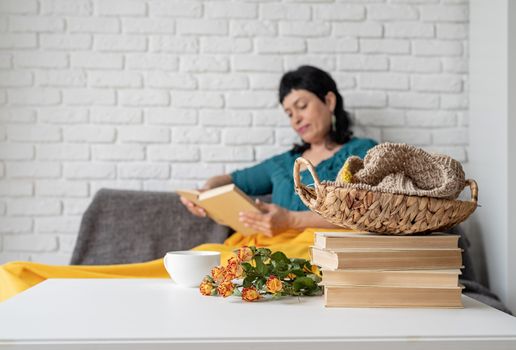 Stay home. Selective focus. Smiling middle aged woman enjoying being at home and reading sitting on the sofe