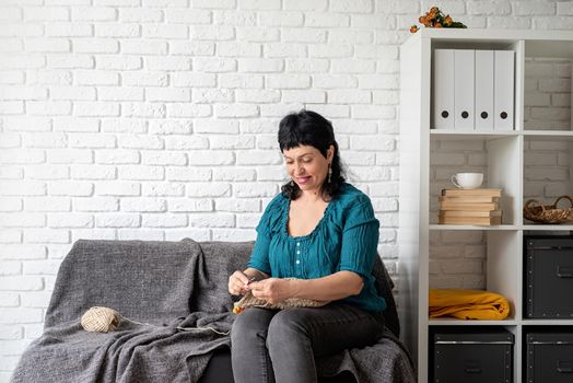 Stay home. Smiling middle aged woman enjoying being at home and knitting sitting on the sofa