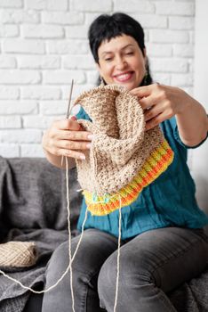 Stay home. Selective focus. Smiling middle aged woman enjoying being at home and knitting sitting on the sofa