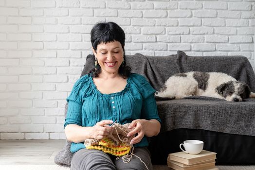 Stay home. Copy space. Smiling middle aged woman enjoying being at home and knitting sitting on the sofa