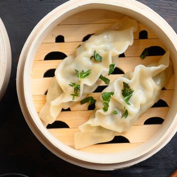 Gyozas potstickers chinese dumplings in wooden steamer with soy sauce fresh herbs and chopsticks on old wood tabletop view overhead close up nobody.