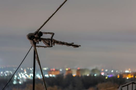 old frozen roof antenna at winter night with selective focus on small city background.