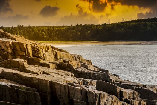 Rocky coastline with golden lights and clouds on sky