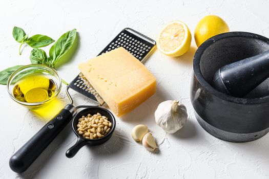 Italian food cooking ingredients on white stone background with Parmesan cheese, basil leaves, pine nuts, olive oil,lemon, garlic, salt and pepper Layout. side view close up.