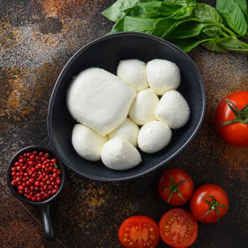 Fresh cherry tomatoes, basil leaves, mozzarella cheese and olive oil on old rustic metal background. Caprese salad ingredients. Selective focus. top view square.