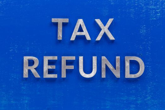 the words tax refund layed on blue painted board with thick silver metal aphabet characters.