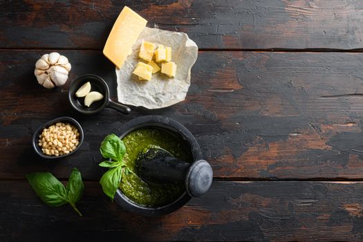 fresh Green basil pesto preparation in black mortar with italian recipe ingredients over old wood table copy space for text overhead