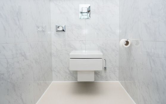Wall mounted minimalist toilet or WC in luxury tiled bathroom with push button flush