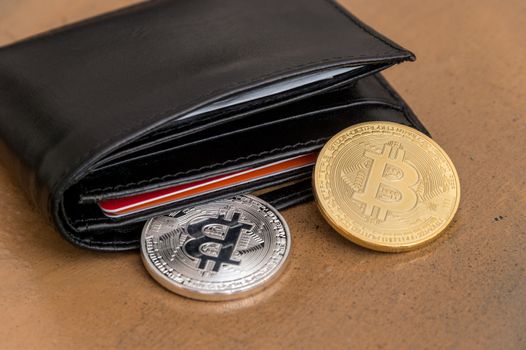 Two cryptocurrency Bitcoin metallic coins coming out a leather wallet