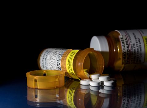 Oxycodone is the generic name for a range of opoid pain killing tablets. Prescription bottle for Oxycodone tablets and pills on glass table with reflections