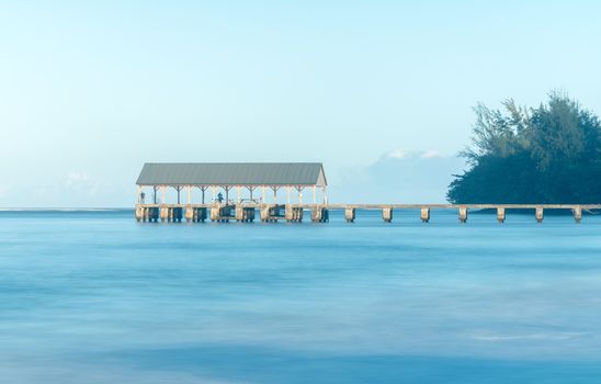 Sunrise lights the dawn sky above Hanalei Pier with long duration exposure to blur waves near Hanalei, Kauai, Hawaii