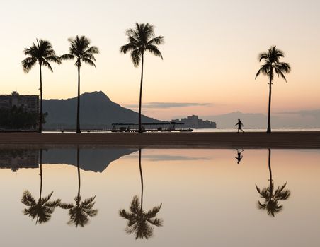 Sunrise in Waikiki with Diamond Head reflected in calm waters of pond as walkers walk along the beach