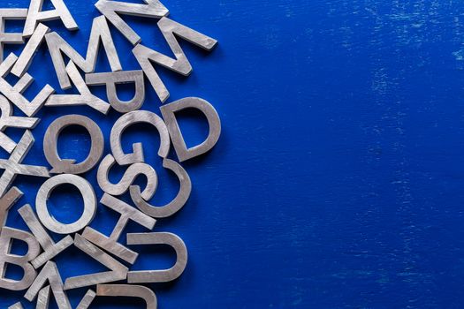 Flat mockup of silver metal alphabet characters on blue painted board background with copyspace. Flat lay abstraction for back to school or language education concept.