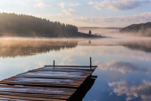 foggy summer sunrise over the river with a wooden pier