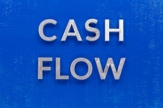 The words cash flow laid on blue painted board with brushed thick silver metal aphabet characters, centered composition concept