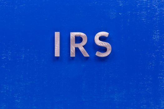 the word irs layed on blue painted board with thick silver metal aphabet characters.