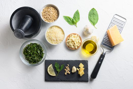 Different ingredients for Italian pesto. Grated parmesan cheese, basil leaves, pine nuts, olive oil, garlic On the white stone slate side top view