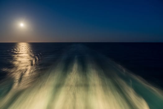 Moon rising over wake and waves of cruise ship at sea with concept of leaving or starting anew