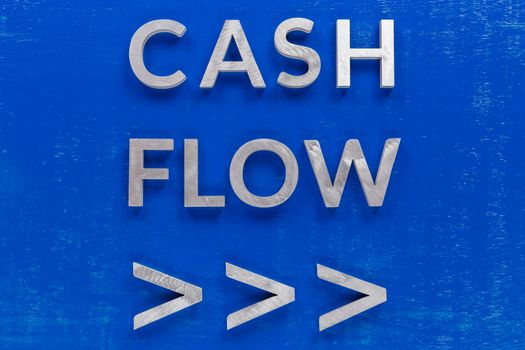 The words cash flow with arrows laid on blue painted board with brushed thick silver metal aphabet characters, centered composition concept