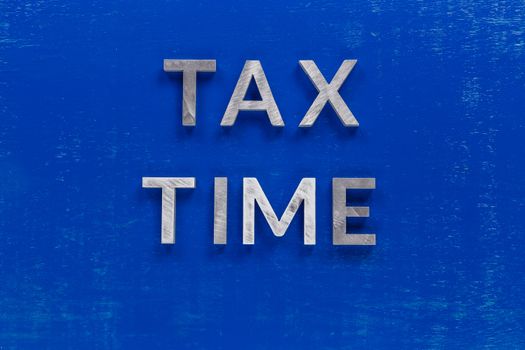 the words tax time layed on blue painted board with thick silver metal aphabet characters.