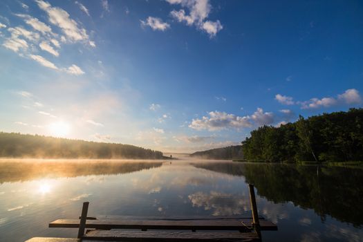 foggy summer sunrise over the river with a wooden pier